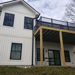 A house with black seamless gutter installed, white vertical siding, and elevated deck, and black-framed windows.